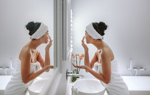 Woman in bathroom applying cosmetic on her face