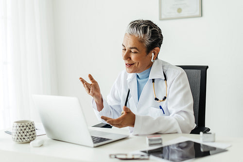 Mature doctor practicing telemedicine in her office, consulting a patient on a video call