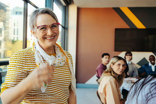 Mature female college lecturer smiling confidently while engaging with diverse students in a modern classroom setting