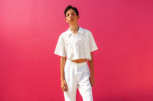 Queer teenage boy standing against a pink background