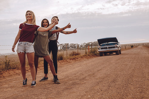 Women hitchhiking near their broken car on country road