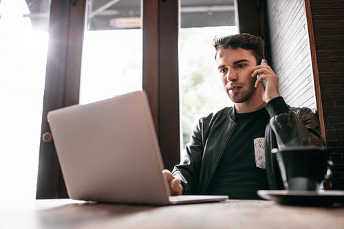 Young man using laptop and mobile phone at cafe