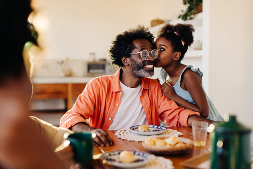 Girl kissing her dad on the cheek at the breakfast table as they dine for a pão de queijo meal