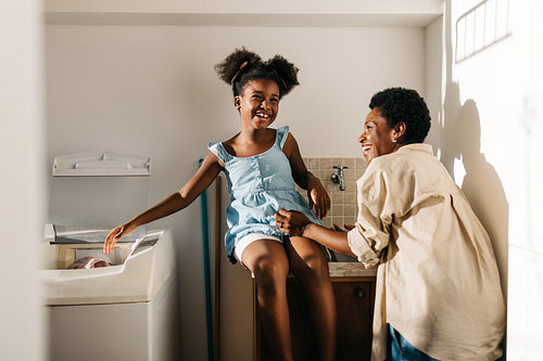Happy mother and daughter doing laundry with a machine at home