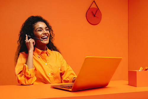 Happy woman working in a vibrant, monochromatic orange office environment, perfect for creative customer service or marketing roles