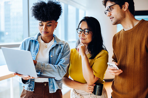Three colleagues review laptop and phone in office