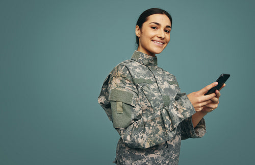 Cheerful female soldier using a smartphone in a studio