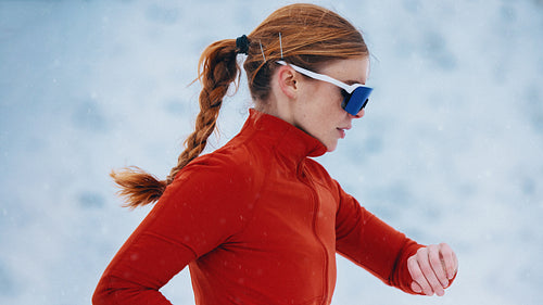 The woman stays focused on her winter running while checking smartwatch data in the snow