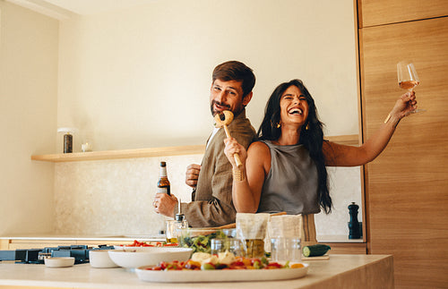 Cheerful couple dancing and singing while cooking in a modern kitchen