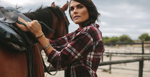 Cowgirl saddling a brown horse