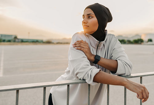 Athletic Muslim woman leaning on a fence outdoors