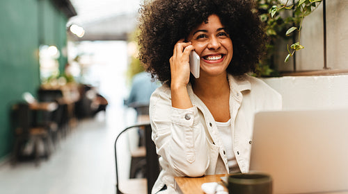 Woman with an Afro smiles as she answers a phone call in a coffee shop