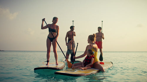 Vacation family enjoy stand up paddleboarding together in the calm ocean during sunset