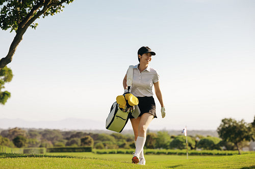 Happy professional woman golfer walking on a sunny golf course