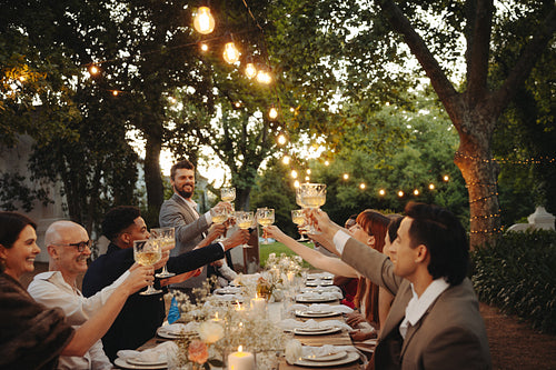 A lively outdoor reception dinner party with friends under sparkling string lights