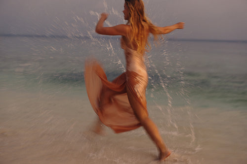 Newlywed bride splashing in tropical ocean at sunset, celebrating romantic beach wedding