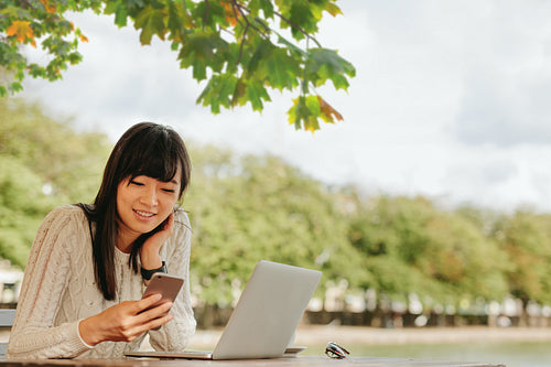 Smiling young woman using mobile phone at outdoor cafe.