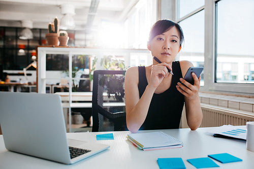 Confident asian woman sitting at her desk with mobile phone