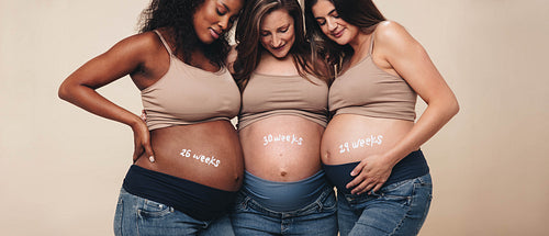 Multicultural women smiling at their pregnant bellies, embracing motherhood in the third trimester
