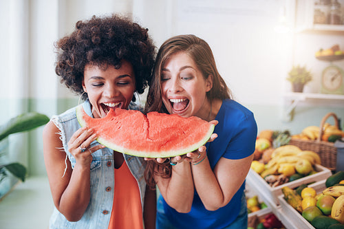 Two women taking a bite of a watermelon