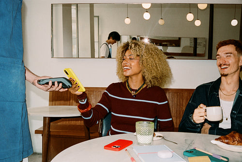 Friends paying for coffee with phone at cafe