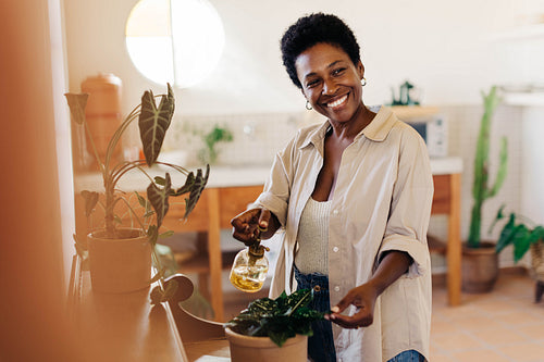 Mature Brazilian woman caring for potted plants with a spray bottle in a green indoor garden plan