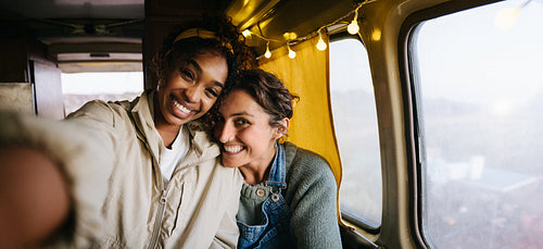 Two friends take a warm selfie inside a cozy bus