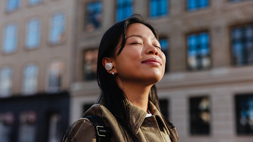 Woman with earbuds enjoying sunlight in city