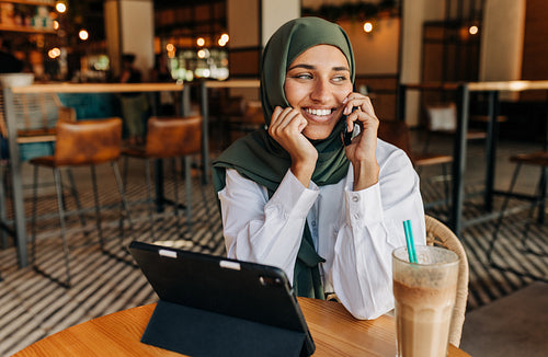 Cheerful Muslim freelancer taking a phone call in a cafe