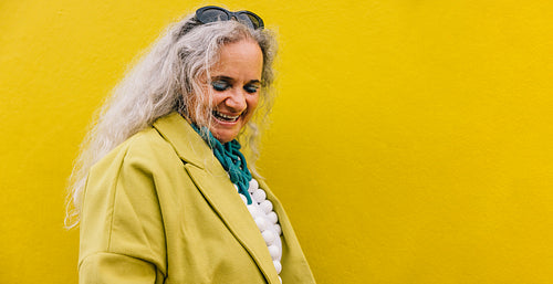Elderly woman smiling cheerfully against a yellow background