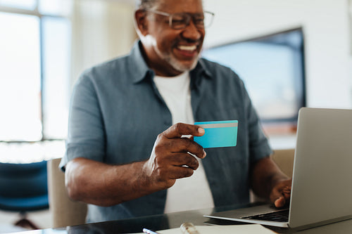 Happy grandfather using bank card for online payment at home
