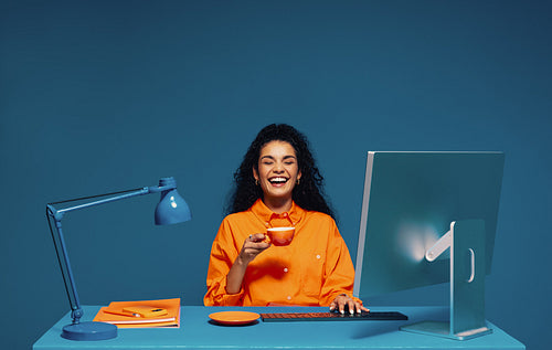 Employee enjoying a coffee break while working at her computer, color blocking studio shot