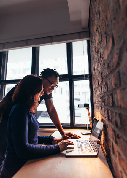 Woman working on laptop with man standing by