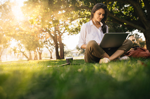 Woman sitting on grass at park working on laptop