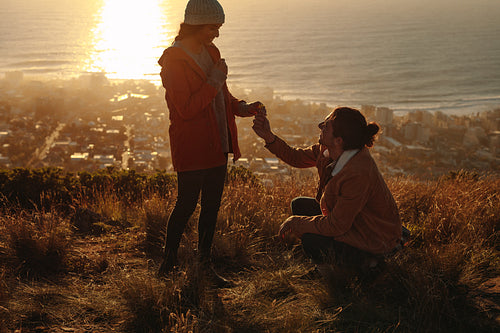 Man proposing woman with wild flower on mountain