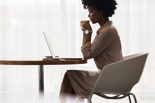 Office worker drinking coffee and looking at laptop