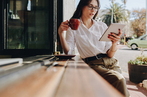 Businesswoman using digital tablet and drinking coffee at cafe