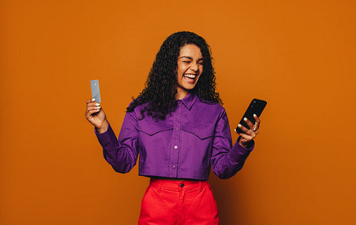 Woman paying with credit card on smartphone, orange background.