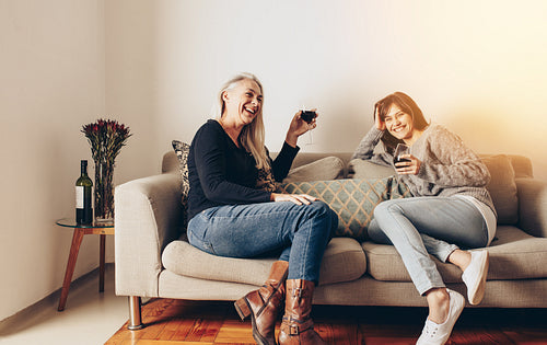 Smiling mother and daughter relaxing on a couch and drinking wine
