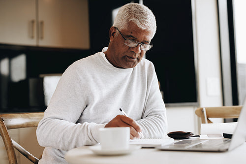 Senior businessman writing notes while working from home