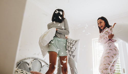 Girls playing with pillows standing on bed