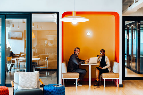 Two individuals discussing work in a booth workspace area