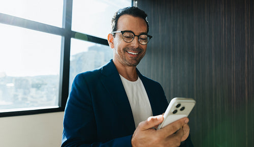 Smiling man uses smartphone for work in bright office