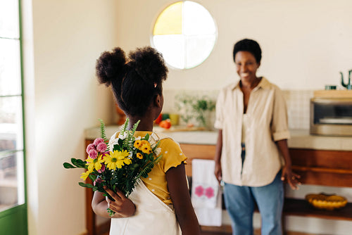 Daughter's loving surprise: Afro-haired girl hiding bouquet behind her back for mom's birthday