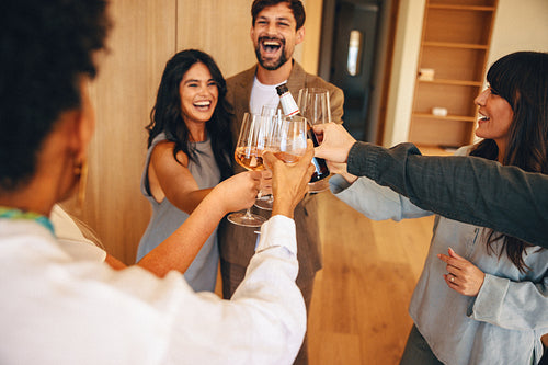 Friends toasting wine glasses at a cheerful celebration inside a cozy home