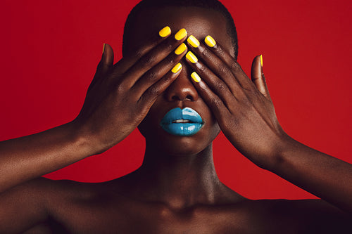 African woman with colorful makeup covering her eyes