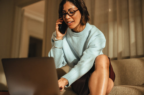 Woman talks on the phone while working on a laptop in her office