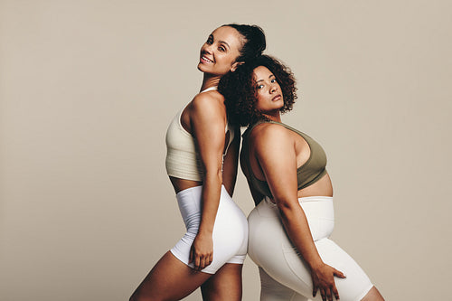 Female athletes show off their toned bodies as they stand back to back in a studio