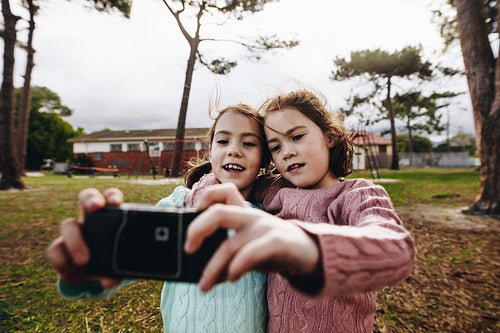 Identical twin girls taking selfie with old camera at park