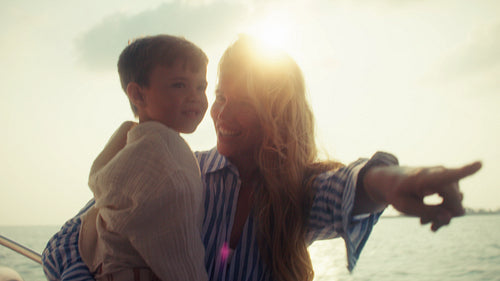 A young mother holding her son on a boat during a beautiful sunset cruise